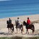 People riding saddled horses on the sand by the water